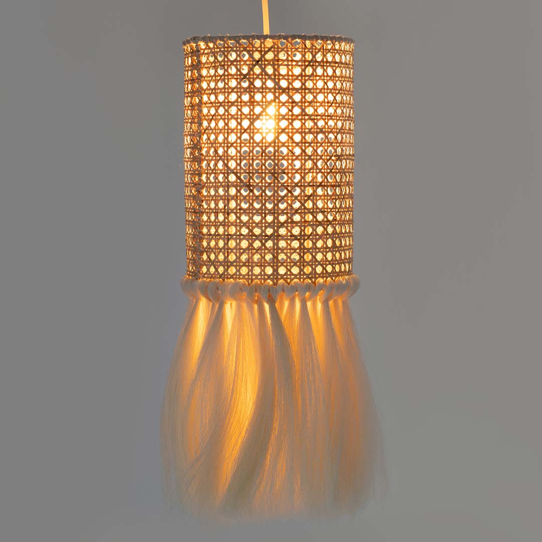 A cylindrical woven rattan lampshade with a sisal fringe hangs from a cord.