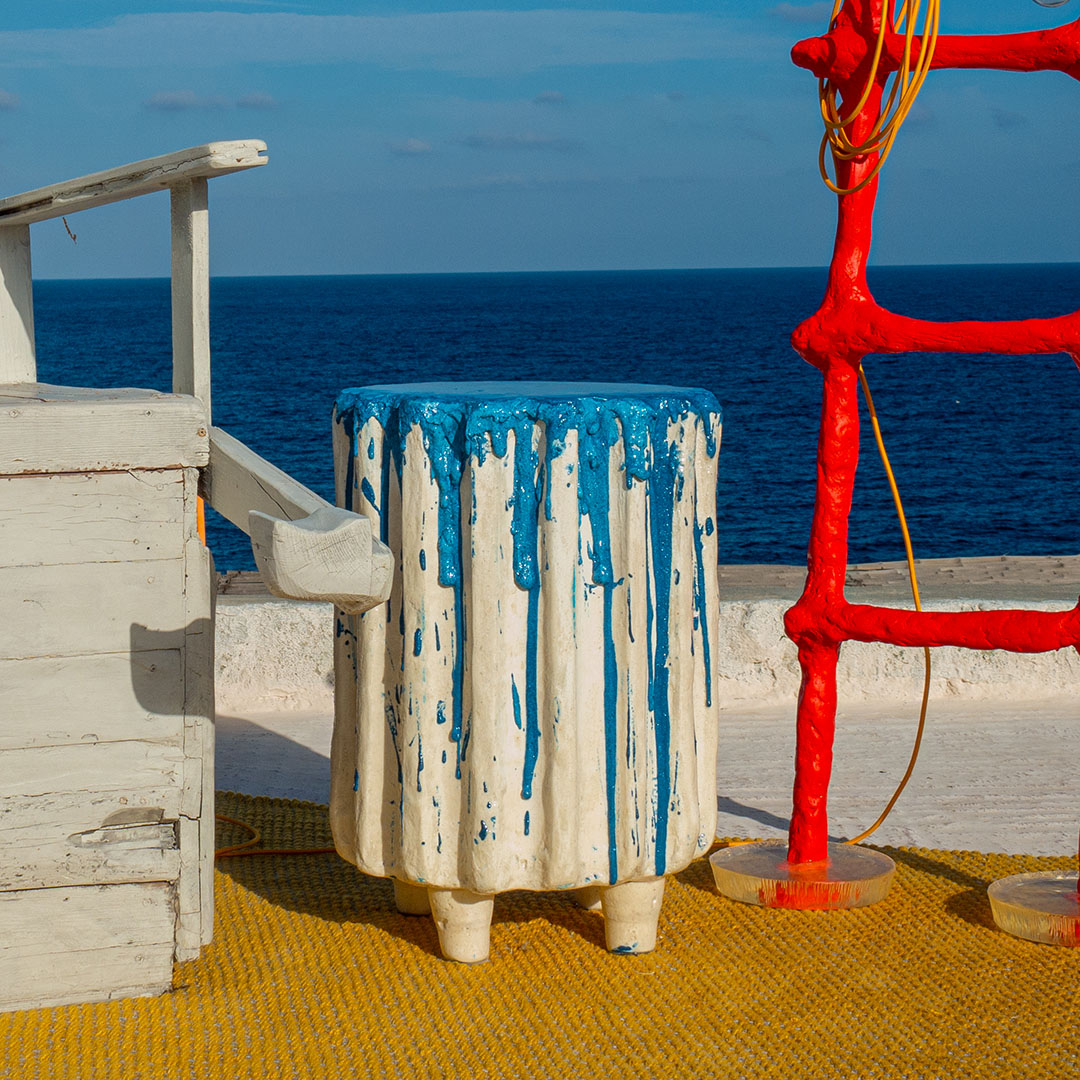 Cake table in between a white chair and a red ladder-lamp