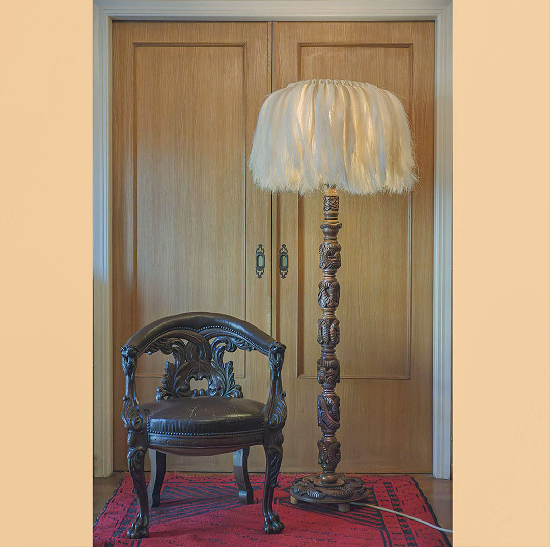 A large floor lamp made from wood and sisal sitting next to a carved wood chair