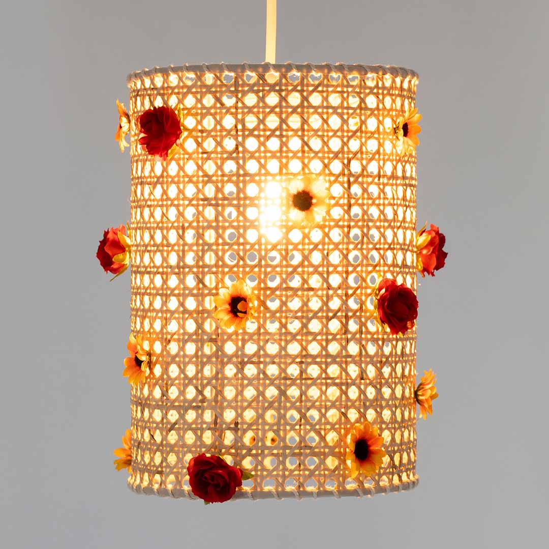 A cylindrical rattan lampshade with red roses and yellow sunflowers, illuminated from within.