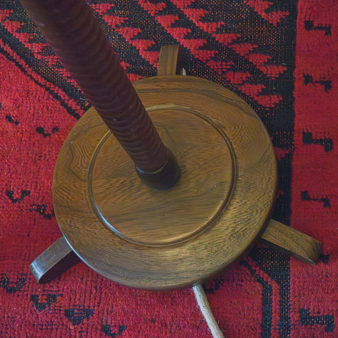 A close-up of the base of a wooden lamp standing on a red and black Persian rug