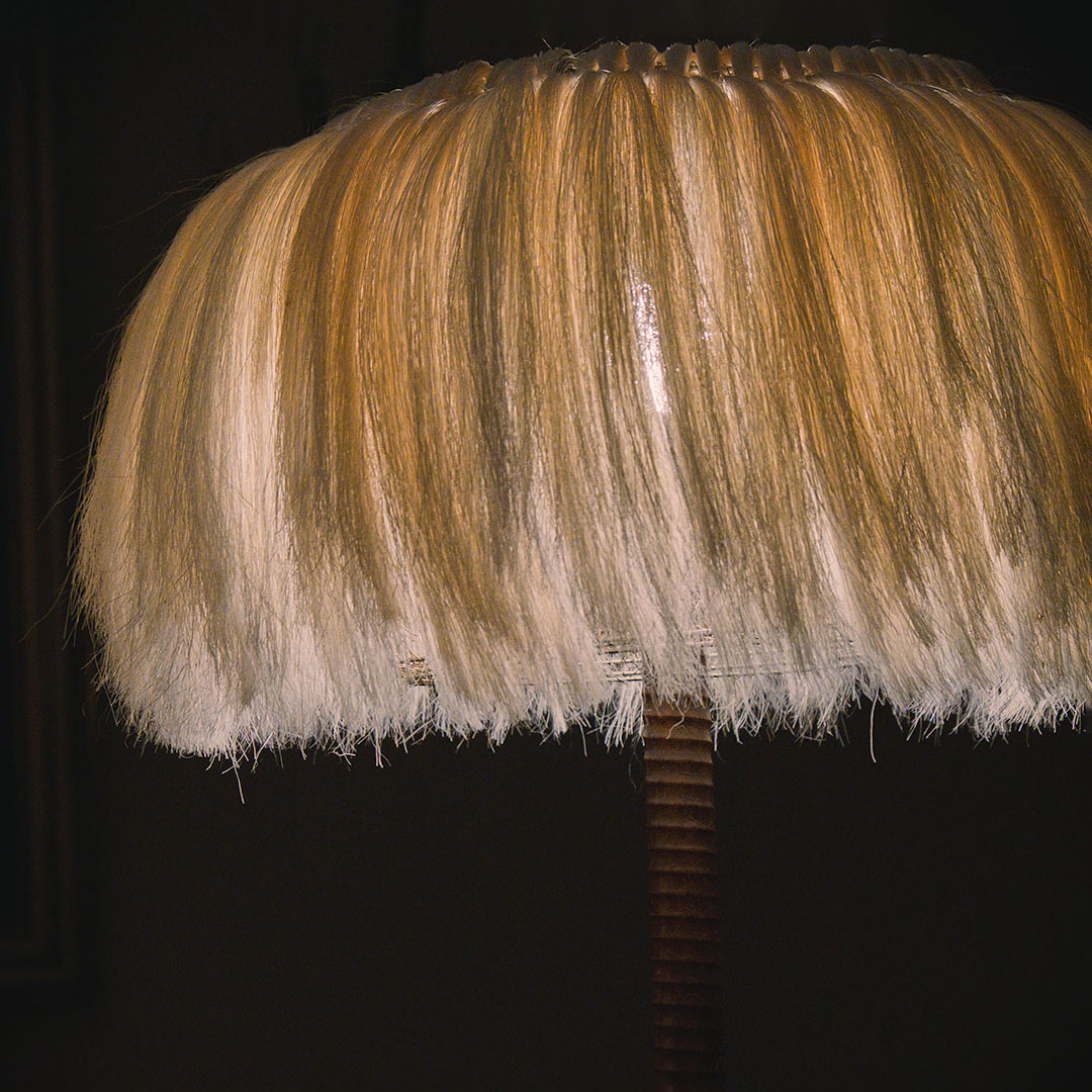 A close-up of a lamp with a hairy shade on a wooden stand in a dark room